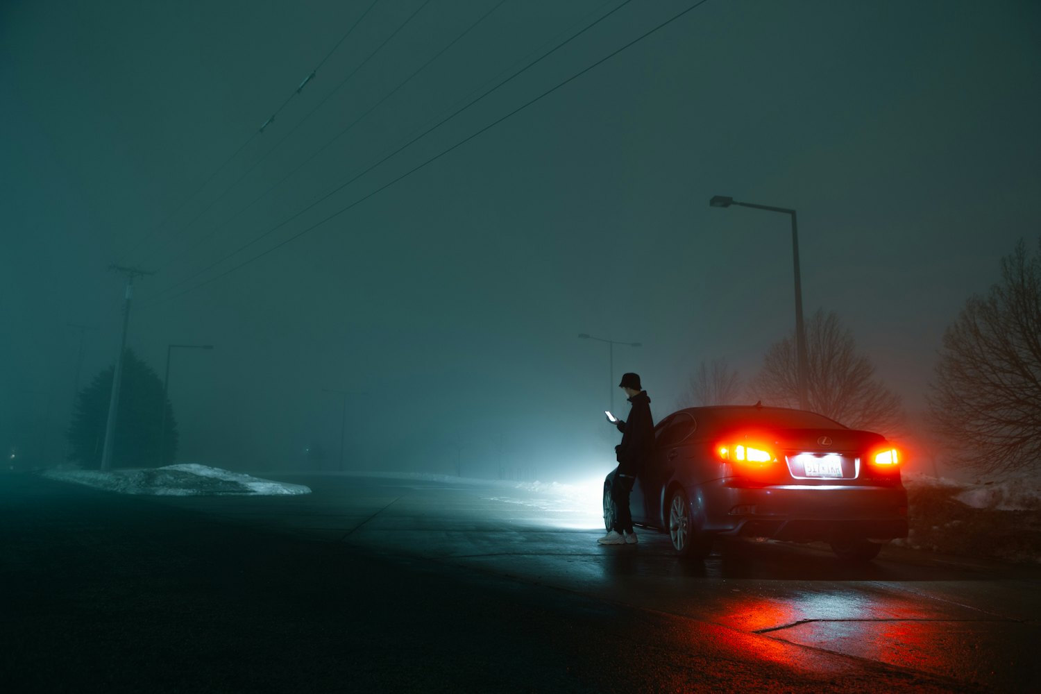 A person alone beside their car on a foggy night