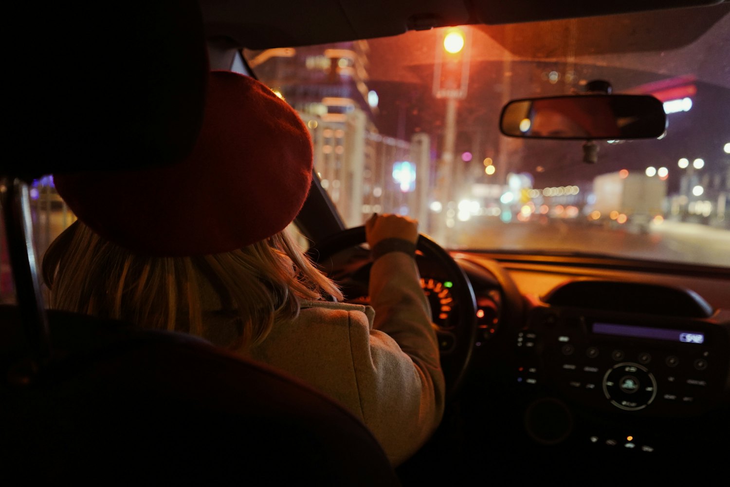 A woman driving through a city at night, lights through the windscreen