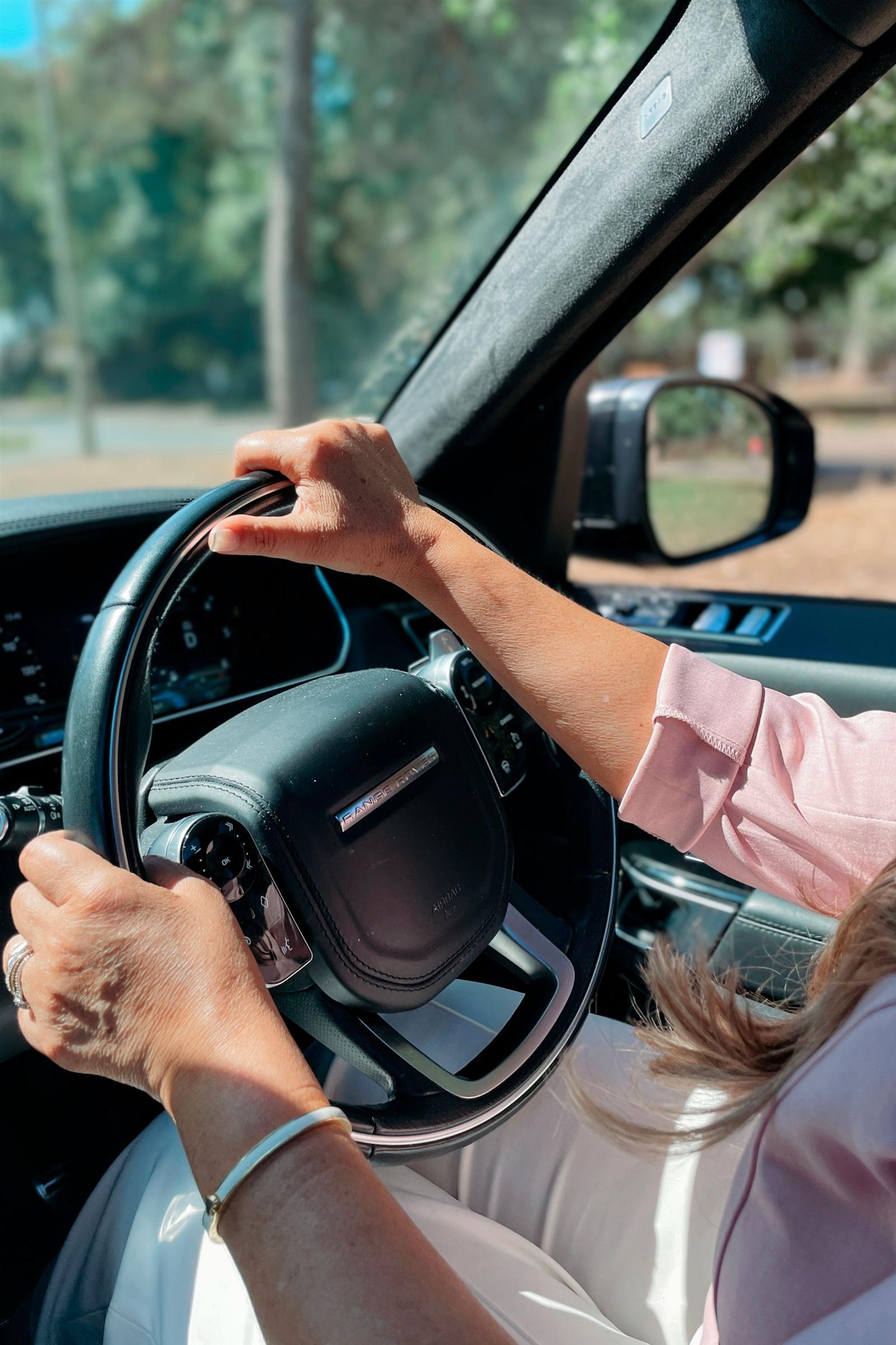 A driver's hands resting confidently on the steering wheel on a sunlit drive