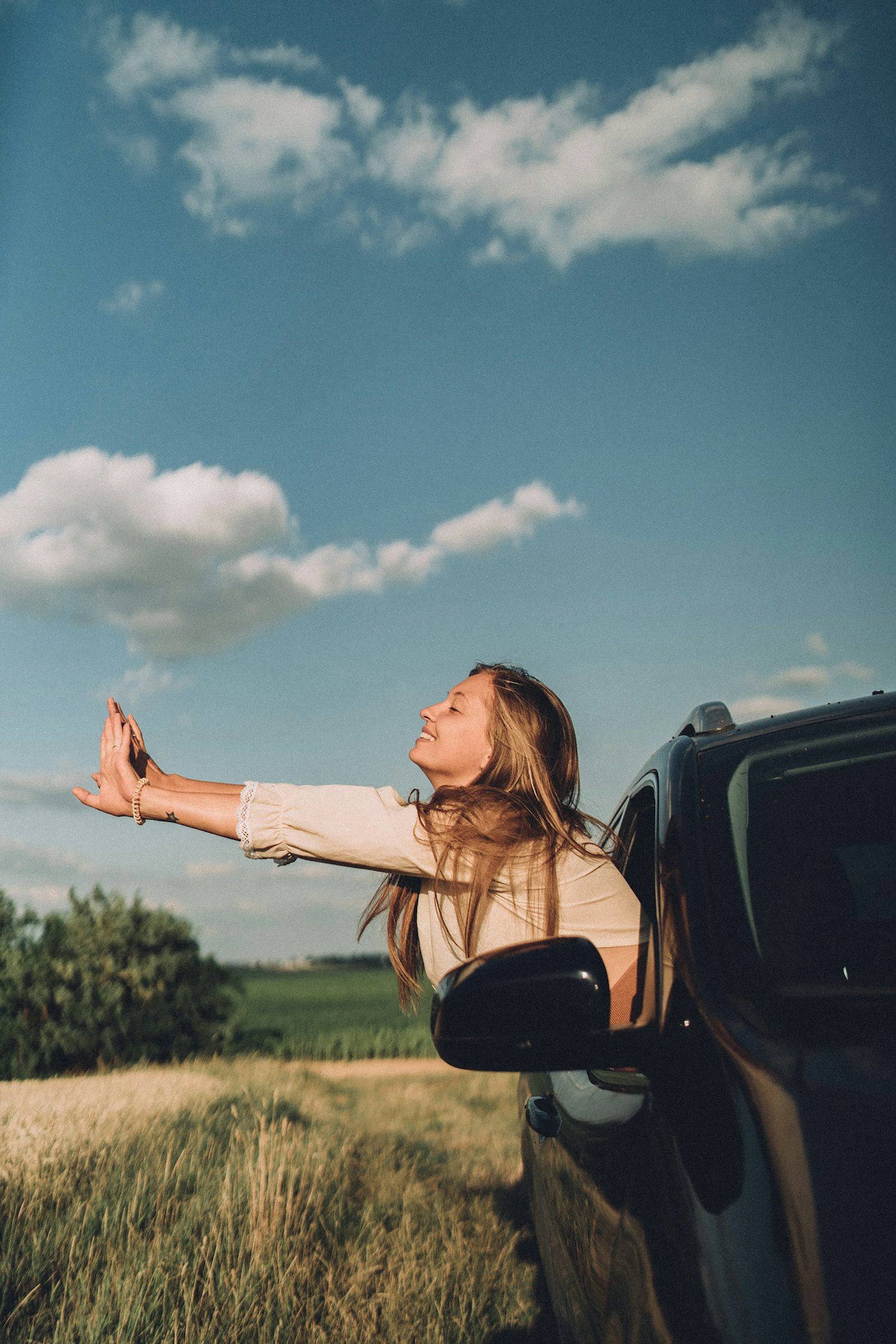 A young driver leaning out of her car window into the sunshine, smiling on a bright day