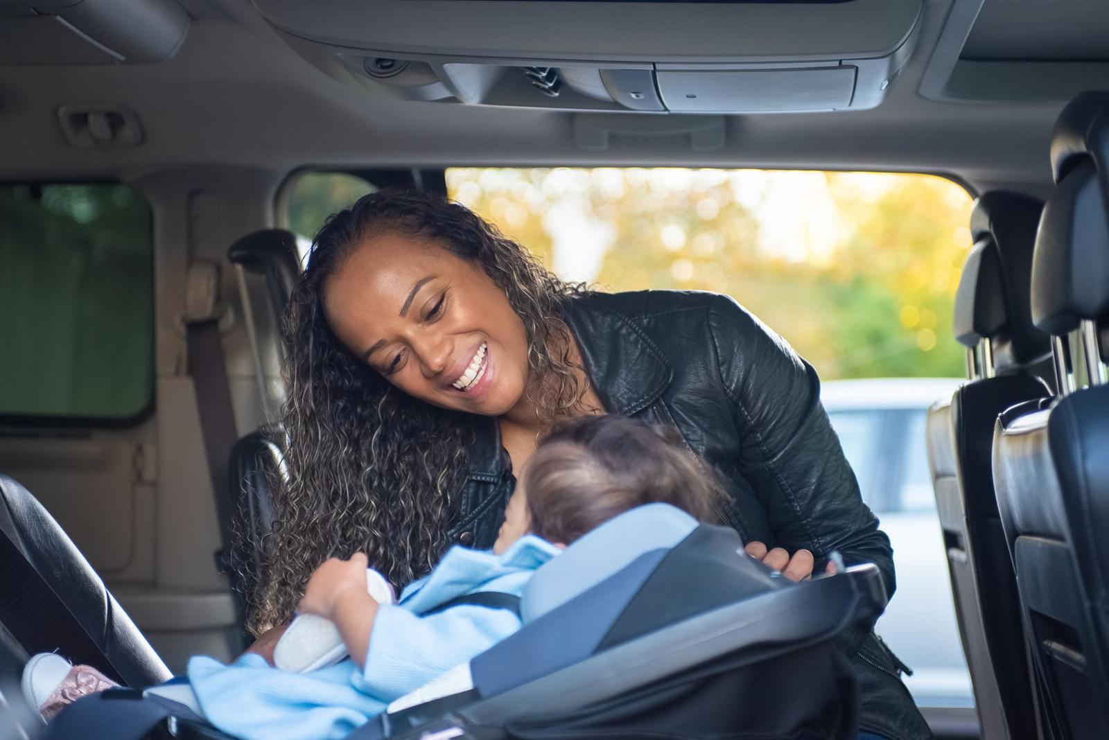 A mother smiling at her baby, safely fastened into a car seat