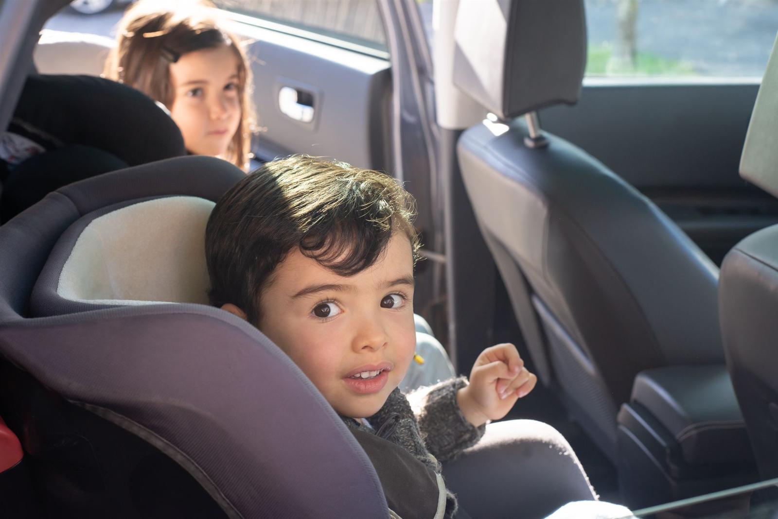 A young boy fastened in his car seat, his sister belted in beside him