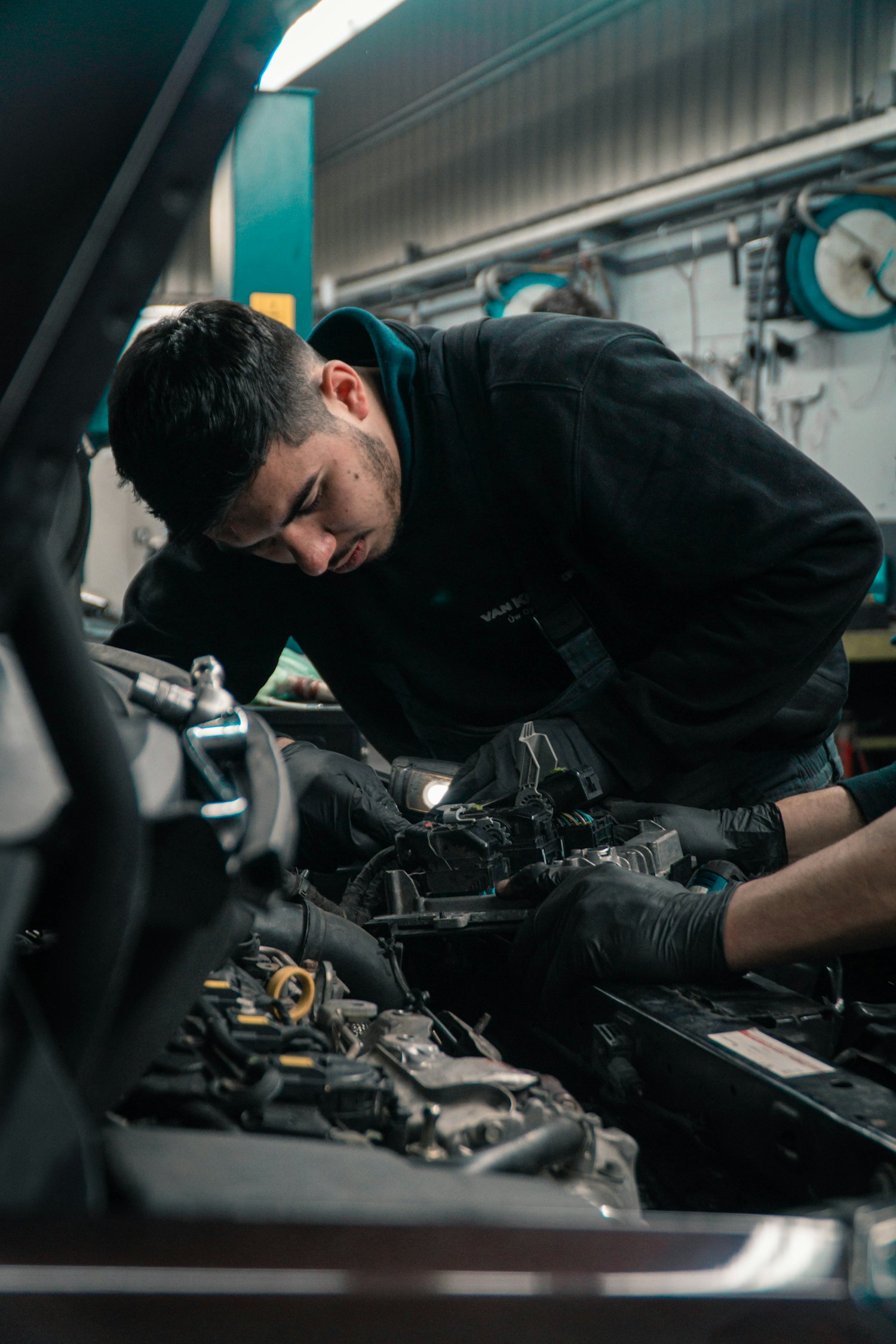 A vehicle technician fitting electronics under the bonnet in a workshop