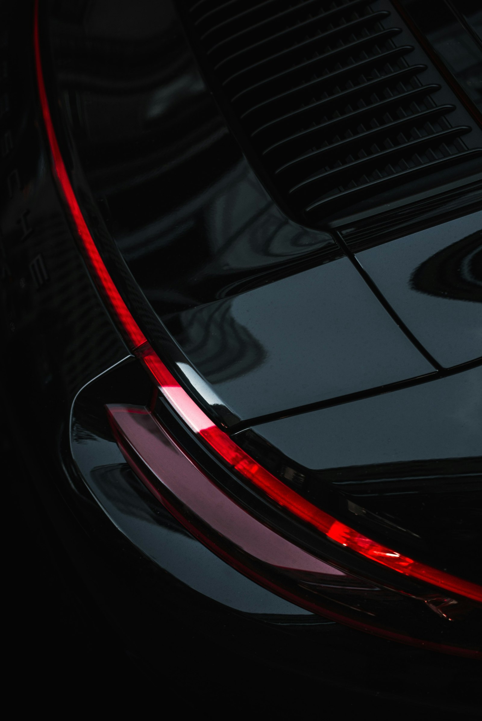 Close detail of a black sports car's rear, a thin red light line tracing the bodywork