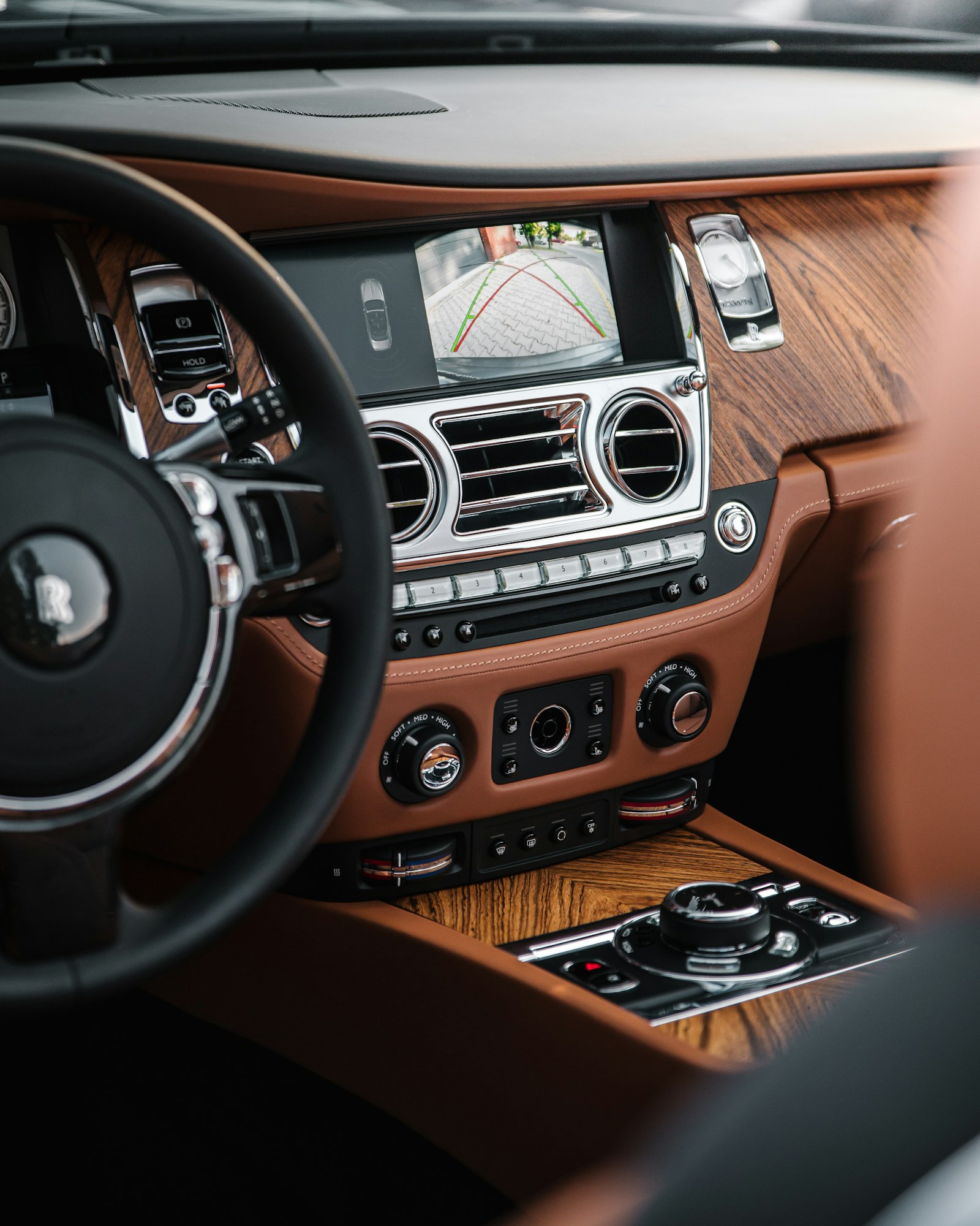 The hand-finished wood and tan leather interior of a luxury car, dashboard and steering wheel in soft light