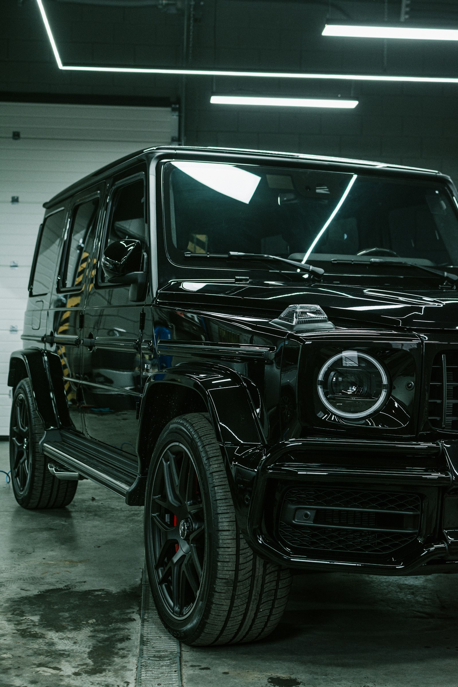 A gloss-black luxury SUV under studio lighting in a detailing bay, paintwork immaculate