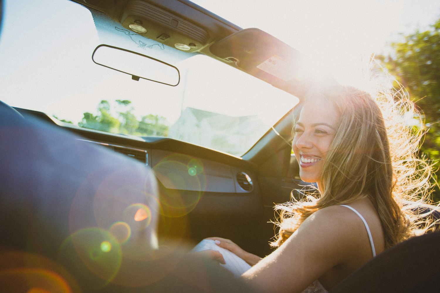 A young woman smiling at the wheel of her car in warm evening light